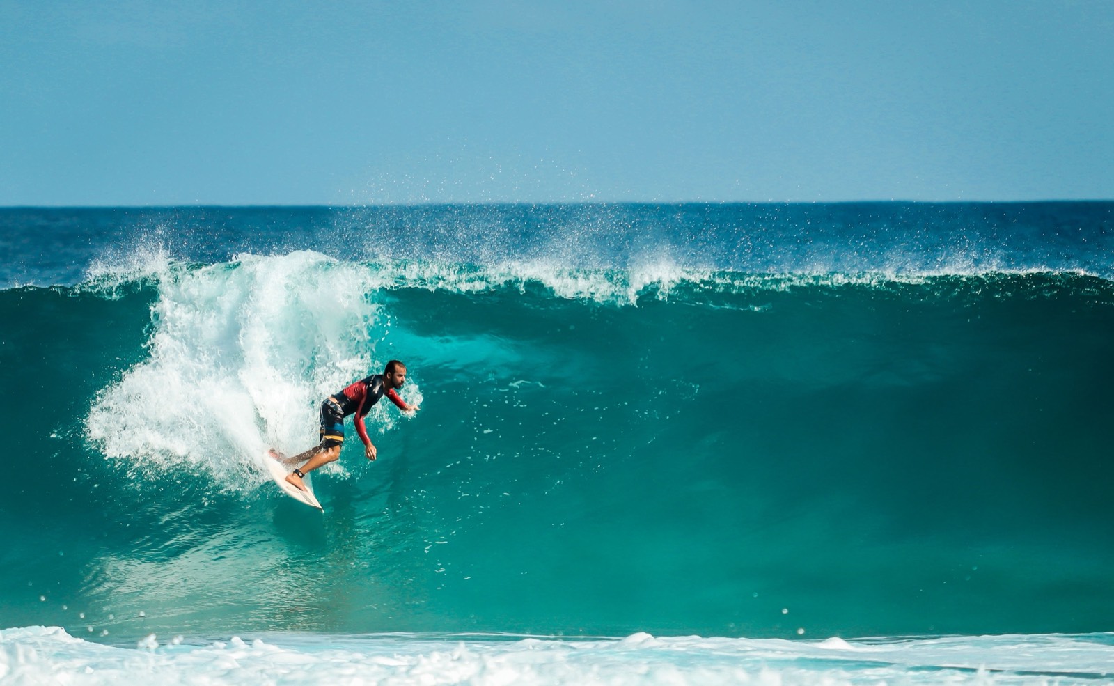 A surfer riding inside a clean blue barrel on a sunny day