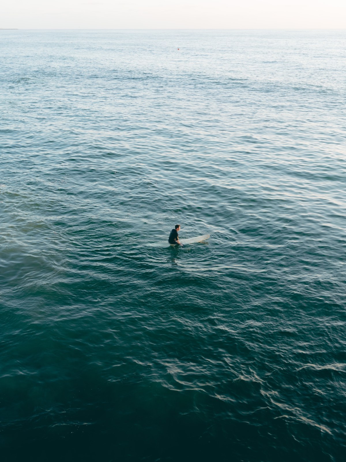 A lone surfer sitting on a board in flat, waveless water